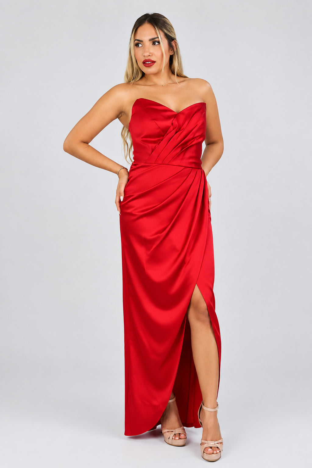 A model wearing a hot red, strapless, V-neck, fitted bodice, and paneled drape style dress.